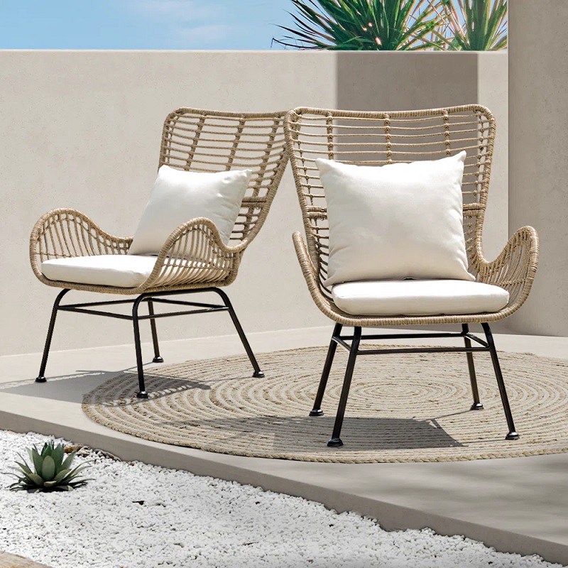 two modern outdoor chairs with wingback shape and white cushions, made from rattan