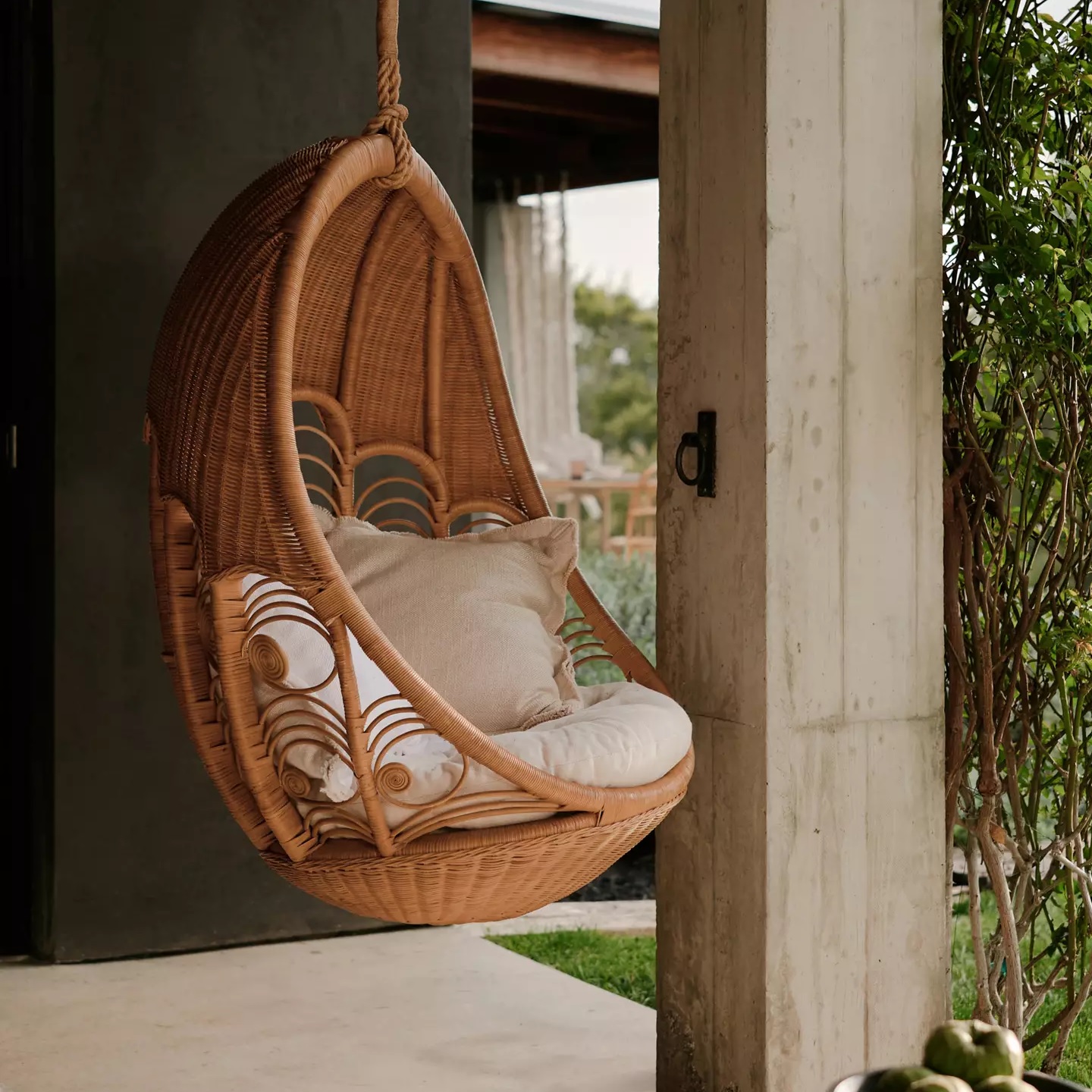 woven rattan swinging chair with decorative flourishes