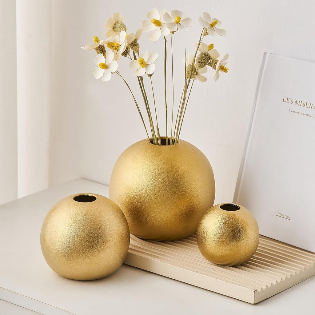 three gold ceramic vases on table with white flowers