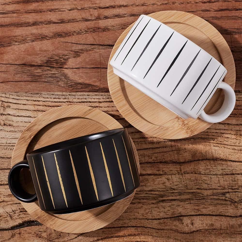 A white and black cappuccino cup on a wood saucer, and a black and gold cappuccino cup on a wooden saucer