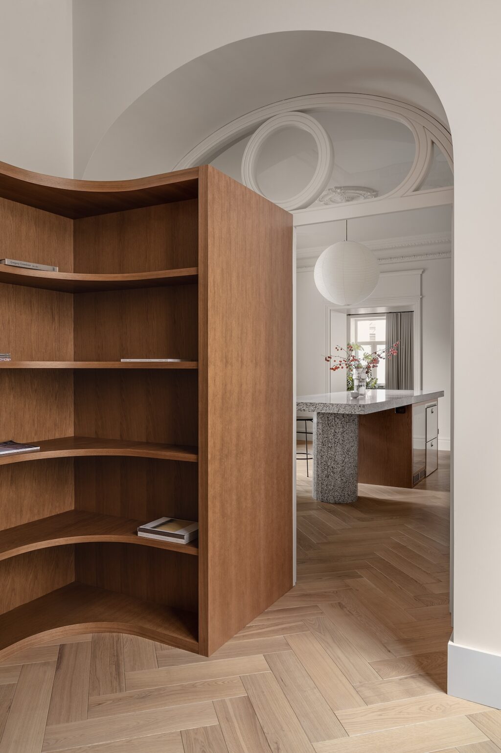 curved wooden bookshelf leading to modern kitchen